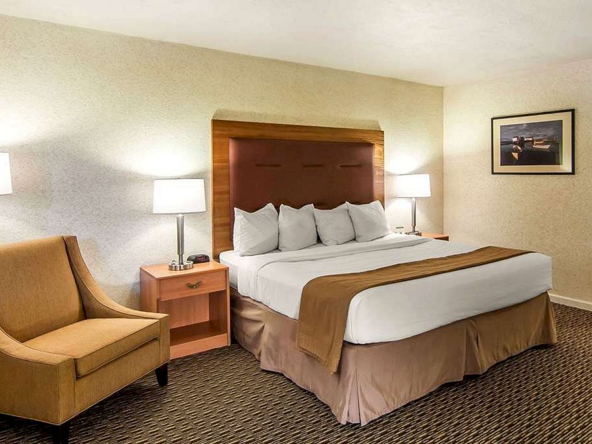 A hotel room with a king-sized bed, two bedside tables with lamps, a beige armchair, and framed wall art in a cozy, well-lit setting.