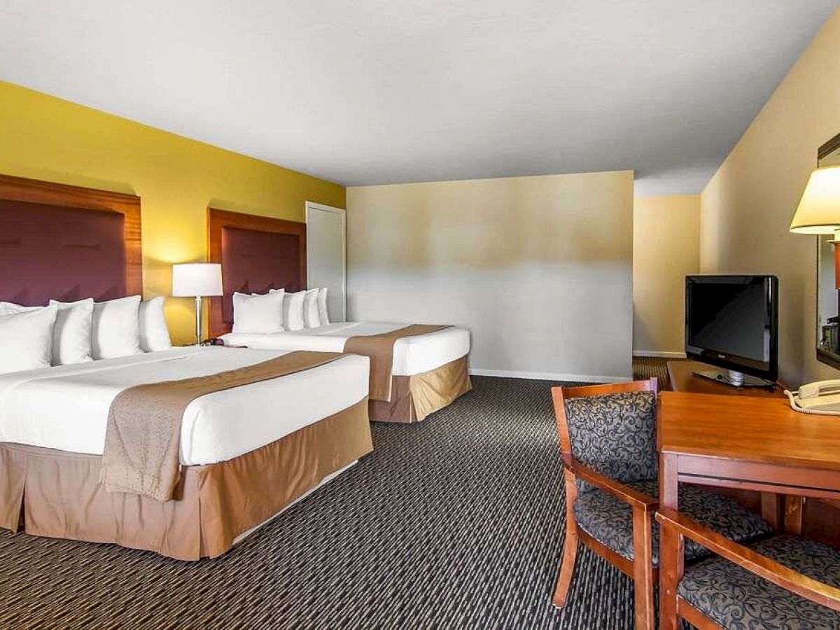 The image shows a hotel room with two double beds, a desk and chair, a TV on a dresser, a lamp, and a mirror on the wall.