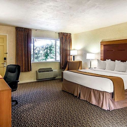 This image shows a hotel room with a large bed, TV, desk, and seating area near the door and window.