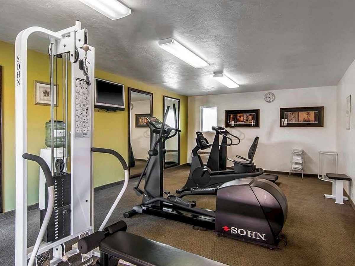 A gym with equipment including a multi-station machine, exercise bikes, and a rower. There's wall art, mirrors, a clock, and a TV monitor.