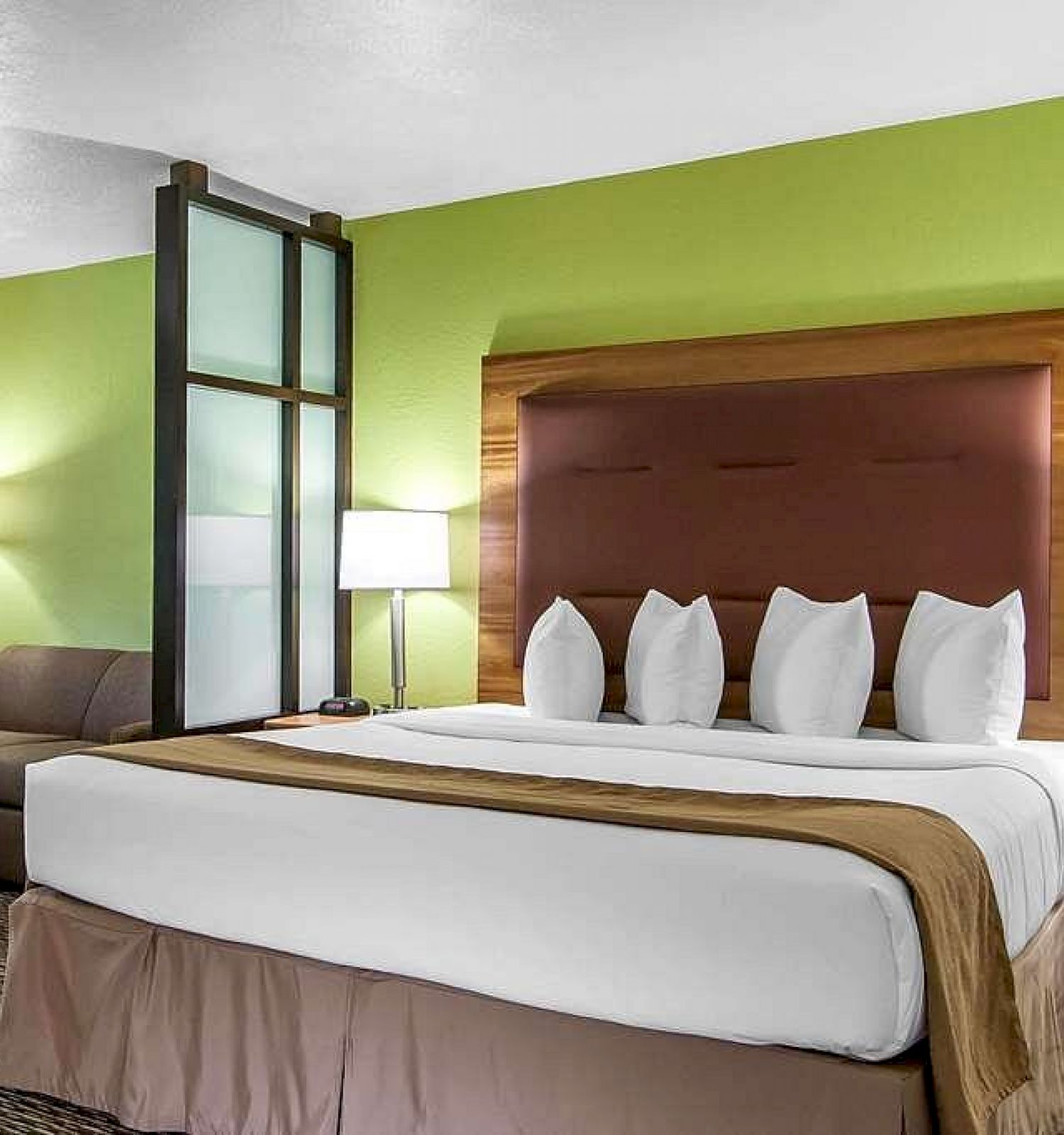 A hotel room with a green accent wall, king-sized bed, nightstands, lamps, sofa, and coffee table, creating a welcoming, cozy atmosphere.