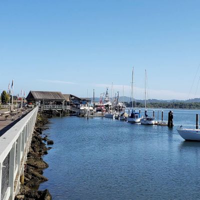 A scenic harbor with docked boats, a wooden pier, and buildings in the background under a clear blue sky, creating a tranquil coastal view.