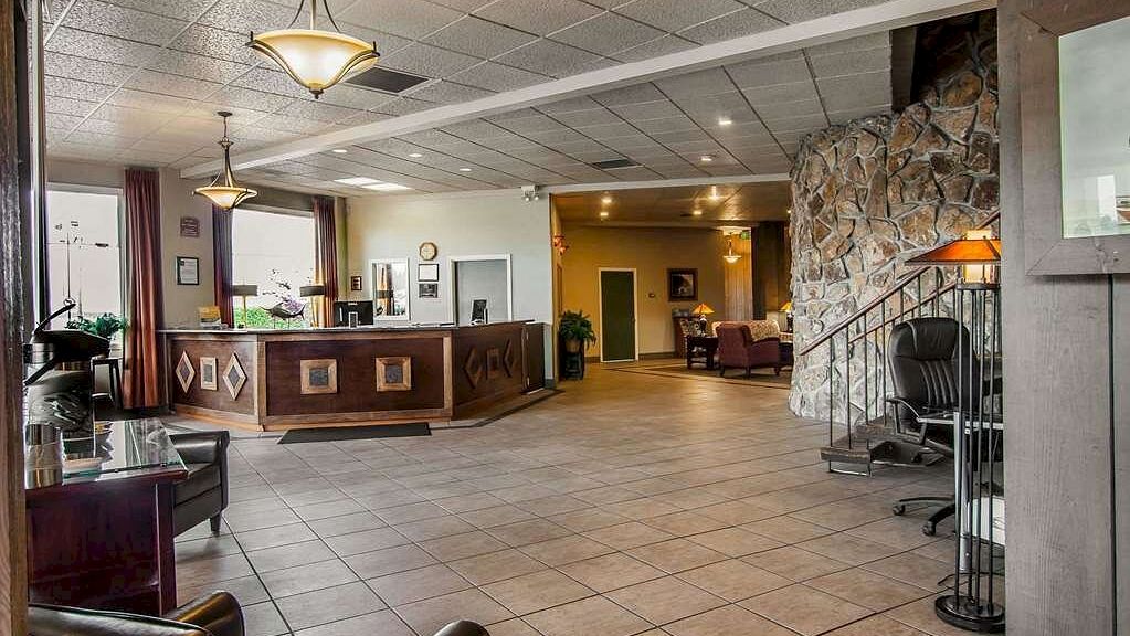 A hotel lobby with a reception desk, seating area, stone wall, and hanging lights. There are armchairs and a desk with a chair on the side.