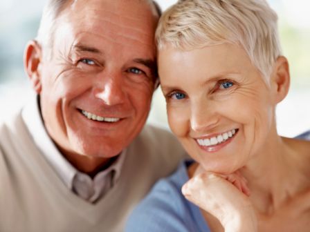 The image shows a smiling older couple posing closely together, with the woman resting her chin on her hand. They appear happy and content.