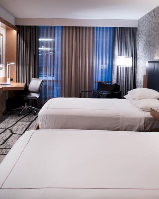A modern hotel room with two beds, a large TV, a desk, a chair, and stylish decor, featuring a combination of wood and contemporary elements.