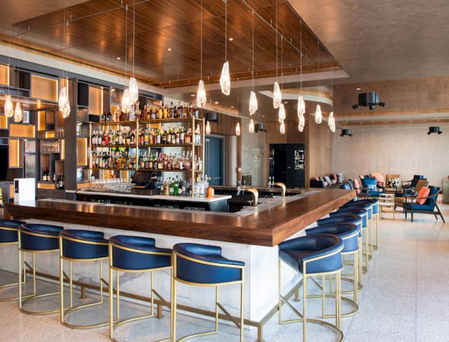 A modern bar with blue and gold stools, a central bar counter, and shelves filled with various bottles of liquor.