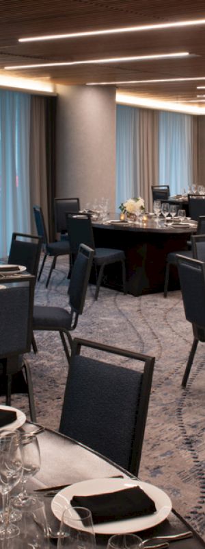 The image shows an elegant banquet hall set up with round tables, black chairs, and neatly arranged dinnerware.
