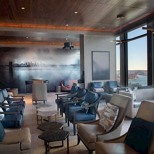 A modern lounge area with ample seating, large windows offering a scenic view of water and a Ferris wheel, and a mural of a city skyline.