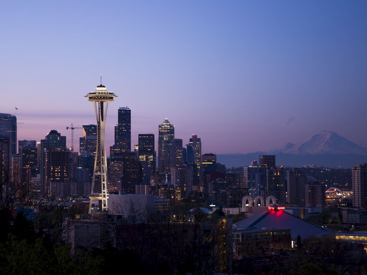 The image shows a city skyline at sunset, featuring the Space Needle, downtown buildings, and a distant mountain.