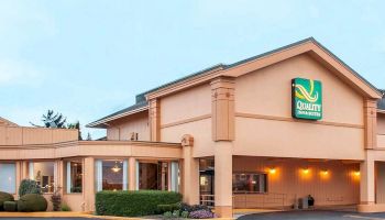 The image shows the exterior of a hotel building with a sign that reads "Quality Inn & Suites." The building has a pale color and is well-lit.