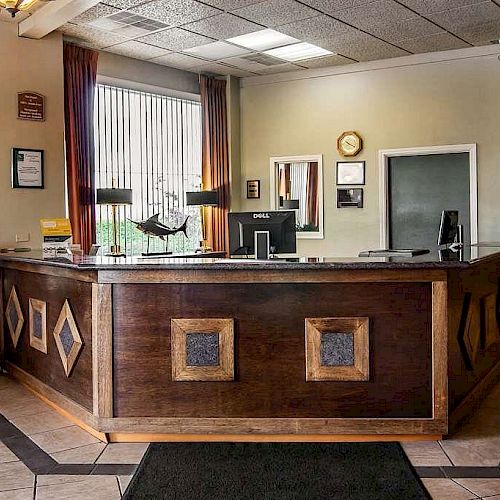 The image shows a hotel reception desk with decorative wood panels, computer monitors, and various framed certificates on the wall.