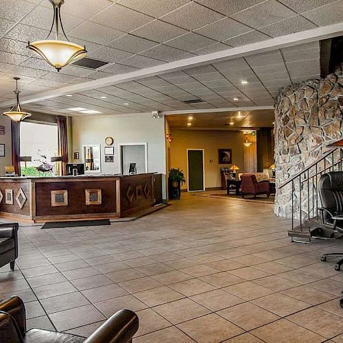 The image shows a hotel lobby with a reception desk, seating area, stone wall, and warm lighting, creating a welcoming and comfortable atmosphere.