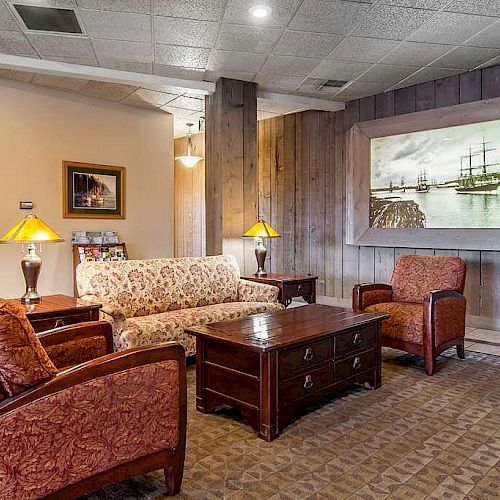 A cozy living room with floral sofa, two red armchairs, coffee table, side lamps, and a framed boat picture on the wall, complete with warm lighting.