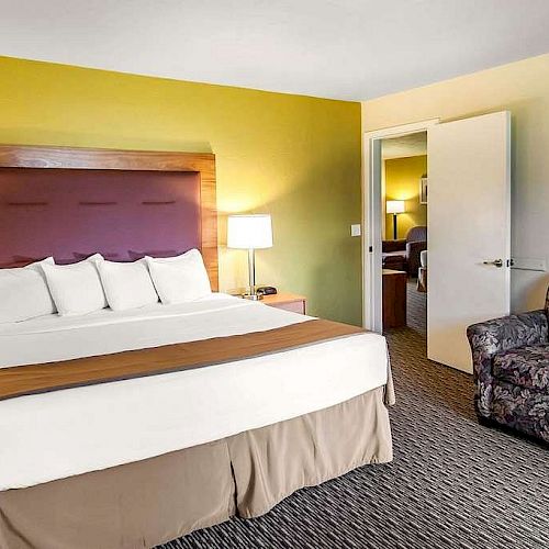 The image shows a hotel room with a large bed, two bedside tables with lamps, a chair, and a mirror. The walls are painted yellow.